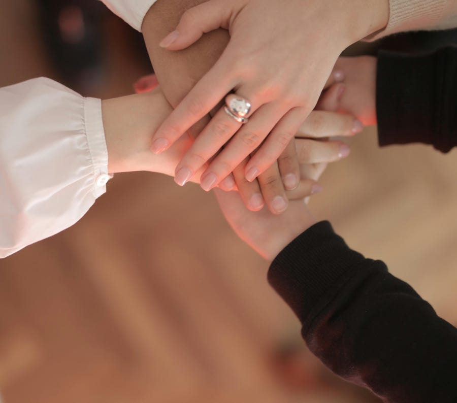 Top view of faceless friends in different clothes stacking hands together while standing on wooden floor indoor on sunny day